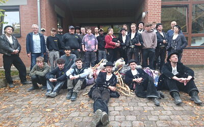 Gruppenfoto der Wandergesell*innen mit Ulrich Mütze, Peter Wilhelm und Auszubildenden vor dem Lehrbauhof Frankenberg.