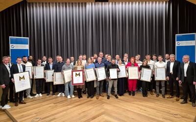 Das Foto zeigt eine große Gruppe frischgebackener Meisterinnen und Meister, die stolz mit ihren Meisterurkunden in der Hand vor der Bühne im Philipp-Soldan-Forum in Frankenberg stehen. Sie tragen festliche Kleidung, einige in Anzügen.