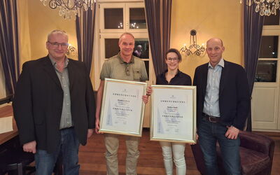 Vier Mitglieder der Innung stehen im Restaurant Friedrichs nebeneinander, zwei halten Ehrenurkunden, alle blicken freundlich in die Kamera.