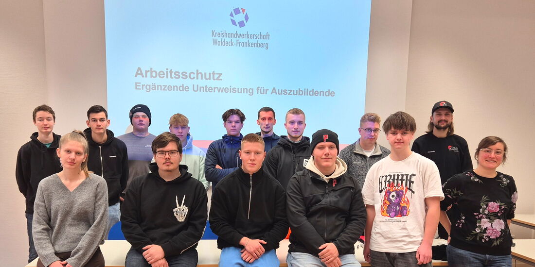 Azubis sitzen und stehen vor einer PowerPoint-Folie. Rechts daneben steht Dozentin Eva Maria Hartmann.