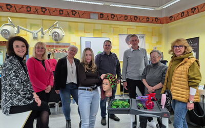 In der Friseurwerkstatt des BBZ in Korbach stehen die Netzwerkpartner des Projekts im Halbkreis um eine junge Fachpraktikerin im Friseurhandwerk im 1. Ausbildungsjahr. Die Fachpraktikerin dreht an einem Modellkopf Lockenwickler auf.
