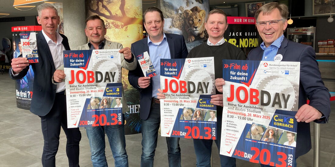 Fünf Männer stehen gemeinsam im Foyer des Korbacher Kinos und blicken lächelnd in die Kamera. Sie halten Plakate und Flyer zum Jobday 2025 in den Händen, um auf die Veranstaltung aufmerksam zu machen.