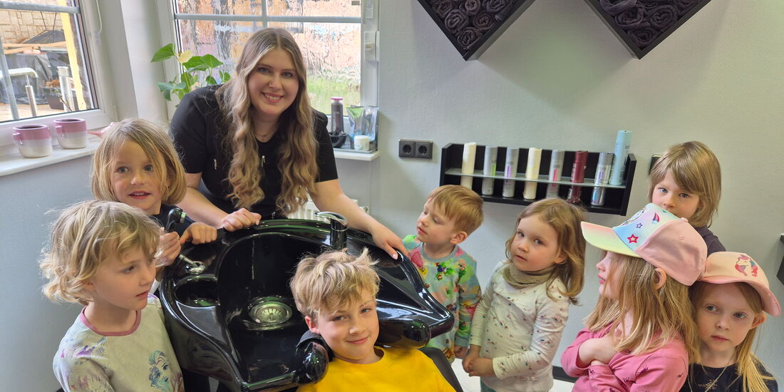 Friseurmeisterin zeigt Kita-Kindern (3–6) den Waschplatz; jedes Kind durfte den Friseurstuhl ausprobieren.