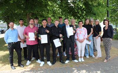 Ein Teil der Absolvent*innen steht mit Lehrkräften im Gruppenbild, alle lächeln – sichtbare Freude nach bestandenen Schulabschlüssen.