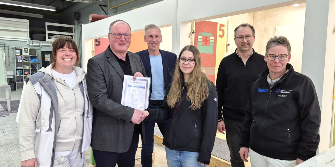 Guido Kalbe überreicht Emily Helmecke in der Malerwerkstatt des BBZ Korbach Urkunde und Scheck.