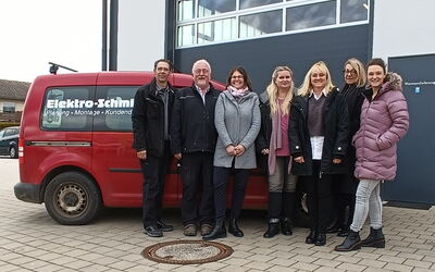 Die Geschäftsführung von Elektro-Schmitz zusammen mit der Abteilungsleitung des BFHs zusammen mit dem Team Plan B und einer Rehabilitandin vor einem roten Firmenwagen der Firma Elektro-Schmitz