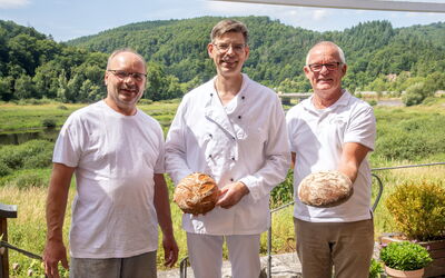 Drei Männer stehen auf der Terrasse der Bäckerei Raabe mit leckerem Brot in der Hand  – darunter der Obermeisterder, Beisitzer der Innung und Prüfer.
