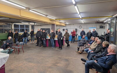Das Foto zeigt eine Gruppe von Menschen in einer Schweiß-Werkstatt. Die Teilnehmenden stehen oder sitzen in einem Halbkreis und hören einem Vortragenden zu. Sie tragen Alltagskleidung. Viele der Zuhörer blicken gespannt auf den Vortragenden.